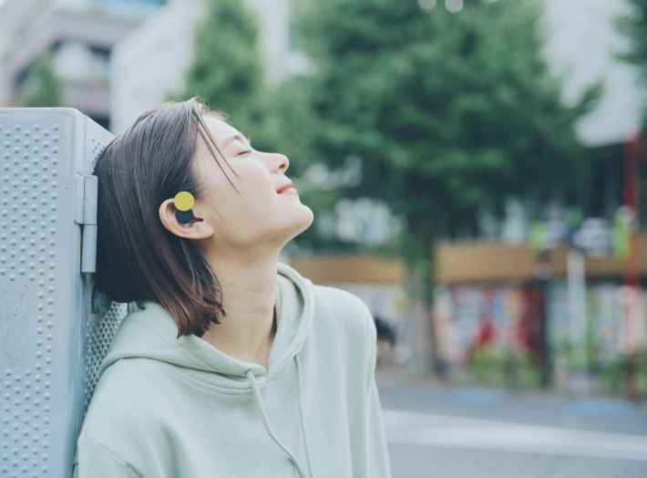 女性がnwmのイヤホンを装着して気持ちよさそうに目を閉じている