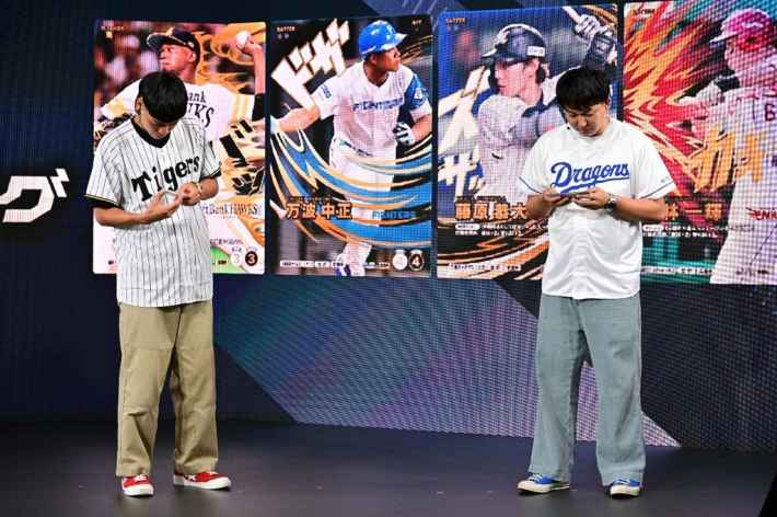 ステージ上でスマートフォンを操作するバッテリィズの二人、背景には選手カードが表示されている