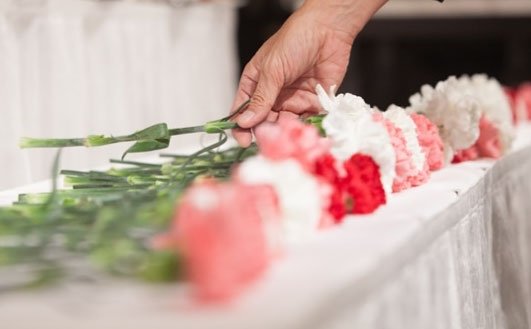 白い花が並べられた祭壇に、一人の手が花を供えている様子。