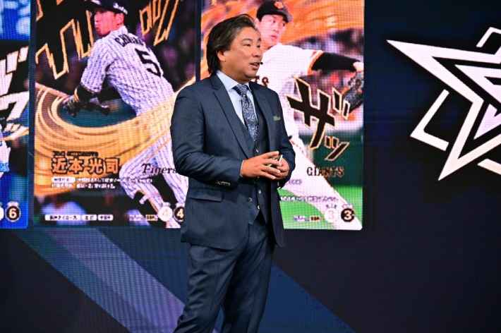 ステージ上でスピーチをする里崎智也さん、背景には選手カードが表示されている